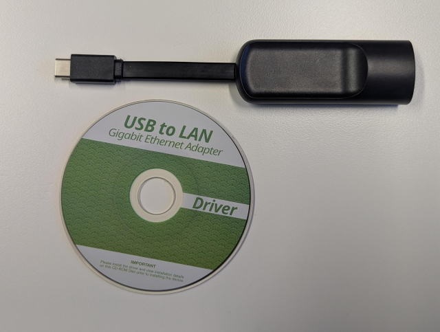 A picture of black USB dongle with type-C plug next to a 8cm CD-ROM with USB to LAN printed on it.