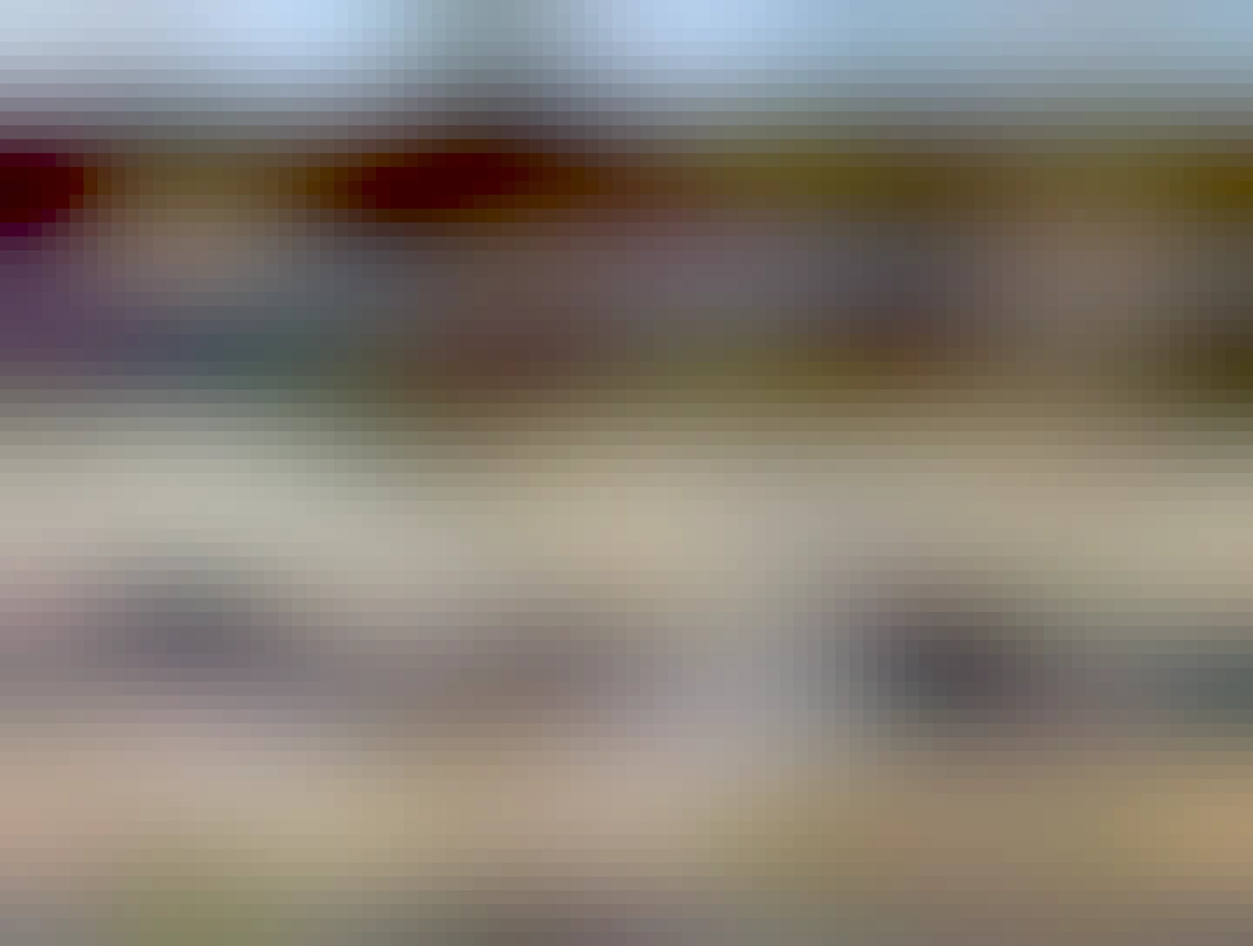 Looking down at a cul-de-sac at a strange scene.  A police car is to the left, lights flashing.  Next to the curb and hydro pole is a hydro truck, with a man in orange checking out the situation with the hydro pole. And...a white car is on the grass between the sidewalk and road, the front end in the air, maybe a 30 degree angle, resting on the guy lines of the pole. 