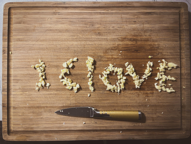 Badly Diced garlic on a cutting board next to a too-small knife. The garlic has been arranged to spell “1 Clove”