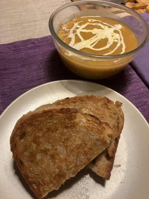 A bowl of butternut squash soup, with a swirl of double cream, and a plate with a cheese and onion toastie