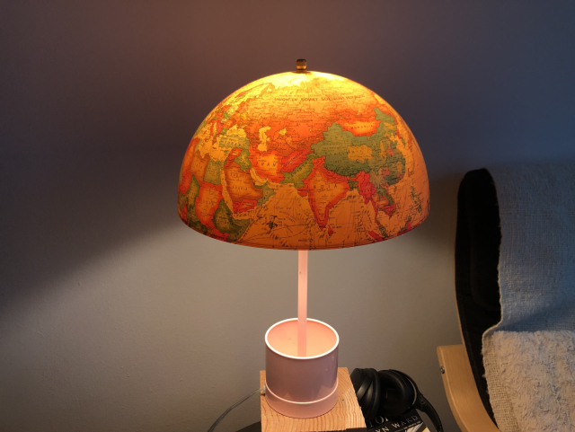 Half of an earth globe is illuminated on top of a pink lap from goodwill, it casts bright yellow pink light 