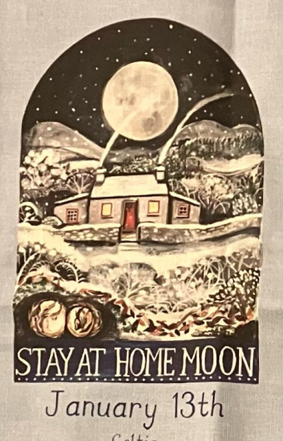 Photo of part of a tea towel that is decorated with illustrations depicting the ‘Full Moons 2025’, this being  tonight’s ‘Stay Home Moon’, a Celtic name. The illustration is a snowy, wintry scene, a cozy country cottage with smoking chimneys below a big bright moon in a starry sky.
