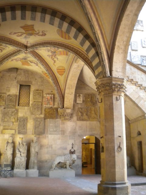 Photo of the inside of the Bargello fortress, with strong pillars and high arches. On the pillars are iron rings for tying up horses, and on the walls are the coats of arms of many nobles who served as the city's chief of police (the Podesta). The fortress also has its own well, in case of siege!