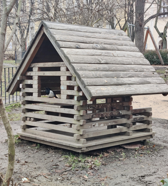 Straka koukající z okýnka dřevěného domečku na dětském hřišti.
