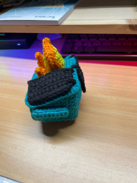 Teal crochet dumpster fire amigurumi on a wooden table
