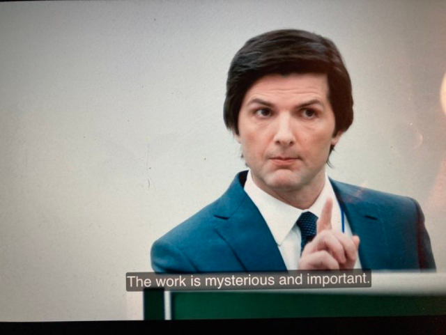 L'acteur de la série Severance en costume bien droit et cheveux bien coiffés sur le coté dit "The work is mysterious and important" en appuyant son propos avec son index levé et un regard appuyé.