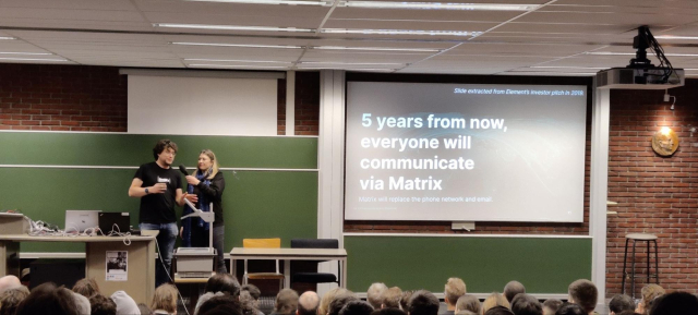 A picture of Matthew & Amandine in front of a captivated audience. Amandine hands the microphone to Matthew. The room is full. The slides read "5 years from now, everyone will communicate via Matrix"