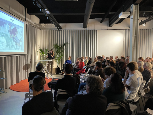 Person is standing and giving a presentation to a group sitting on chairs