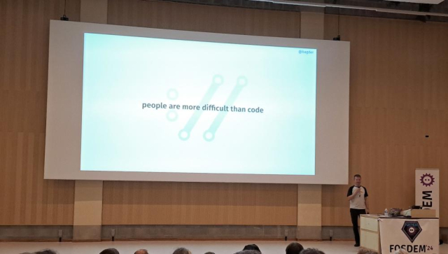 A projection screen at a talk with text "people are more difficult than code"