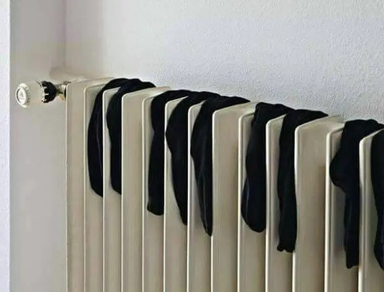 Black tights hanging over a beige radiator, with a decorative valve at one end, against a simple white wall background. The impression is one of the black keys amongst the white keys on a piano