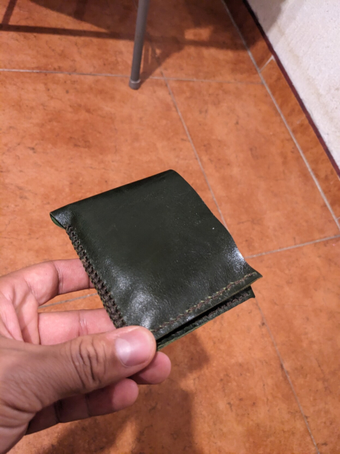 La cartera cerrada, luciendo su fina piel color verde oscuro y los dos tipos de puntadas que tiene