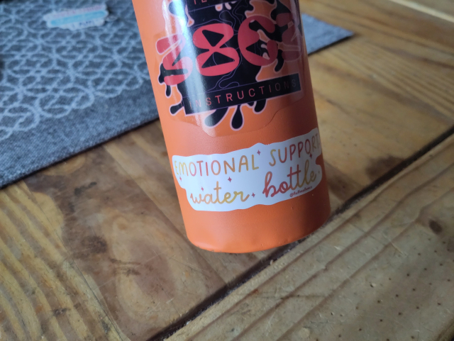 An orange water bottle with a sticker that says: "Emotional support water bottle"