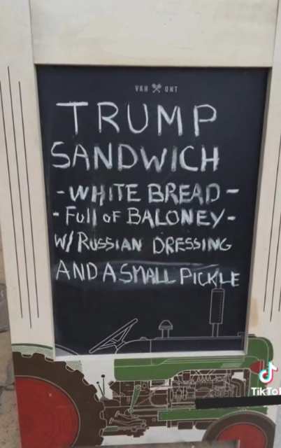 A chalkboard menu sign outside a restaurant says: Trump Sandwich: White bread, full of baloney, with Russian dressing and a small pickle.