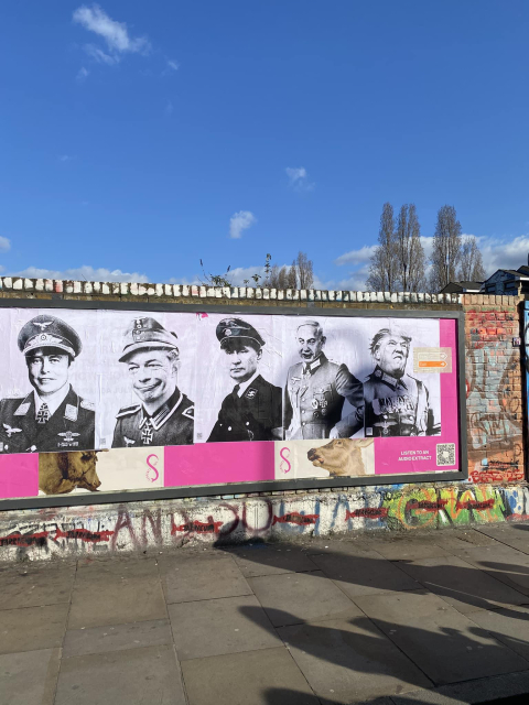 A controversial street art installation on a wall in Brick Lane, London, featuring a series of black-and-white portraits of historical Nazi officers, with one edited to include the face of Elon Musk, Nigel Farage, Vladimir Putin, Benjamin Netanyahu and Donald Trump. The artwork is pasted on a pink and white background with an image of a cow. The surrounding wall is covered in graffiti, including spray-painted words and colorful tags. The sky is clear and blue, with shadows cast onto the pavement by passersby.