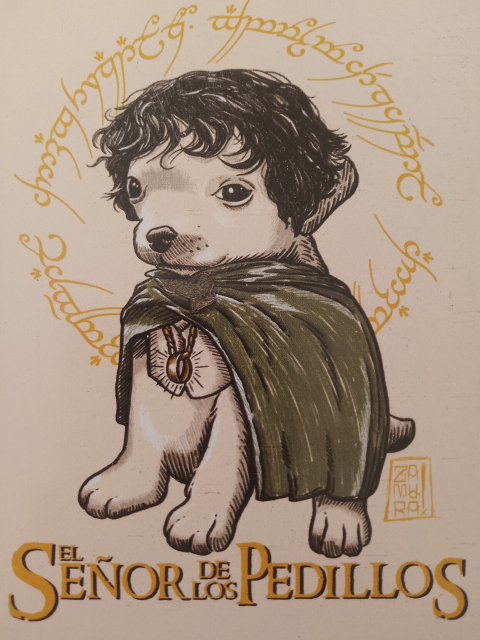 Ilustración de un cachorro de perro con peluca negra y una capa verde. Trae colgando un collar con un anillo dorado. Atrás del perro hay un círculo de caracteres élficos de "el anillo único". Debajo del perrito está escrita la leyenda "El Señor de los Pelillos".