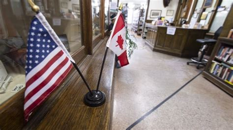 Photo of Haskell Free Library and Opera House. A library with a border on the floor. Two flags Canadian and American sit on a book case above the line marking the border between the two countries. In the background books and a desk like any other library.