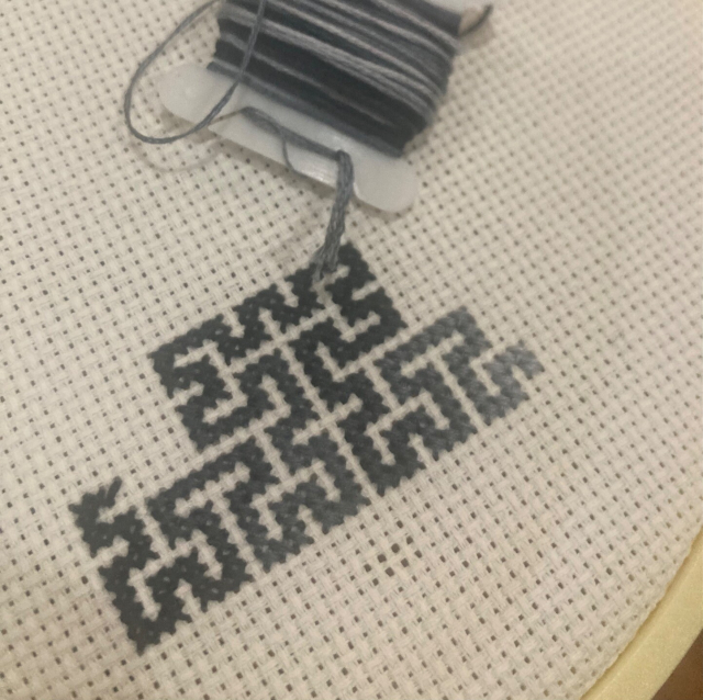 A cross-stitched Hilbert curve that fades between light and dark gray