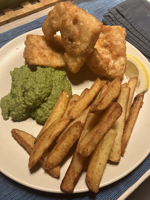 A plate with battered fish, triple cooked thick cut chips, and a generous dollop of mushy peas