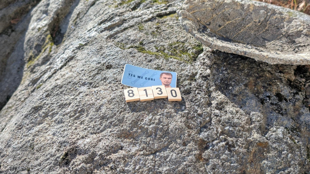 A rock on which there's a sticker saying "yes we curl" and four wooden tiles with the numbers 8, 1, 3 and 0 on them.