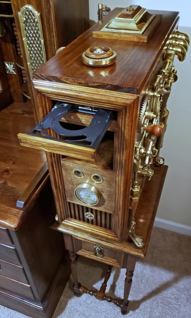 A fancy wooden computer case with brass components, knobs on gears, and a pressure/temp value on the front. The walnut colored wood chassis matches the office desk next to it and the side table that it rests upon. An optical disc drive tray is open as if waiting for 20,000 Leagues Under the Sea to be loaded.