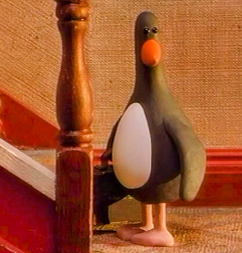 The Feathers McGraw character from Wallace and Gromit, standing at the bottom of a staircase, carrying a briefcase.