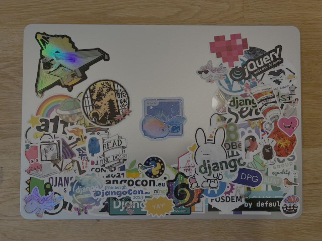 Picture of a metal laptop with stickers all over. From top left to bottom right, we see the JWST, a a11y rainbow, an octopus, a blue bird, Read the Docs, the Django pony, DjangoCon event stickers, Yay, EuroPython, the Django Girls heart, jQuery, moomin, PDBe