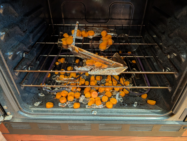 The inside of an oven, with pieces of glass everywhere after a casserole dish exploded. Carrot pieces are also everywhere