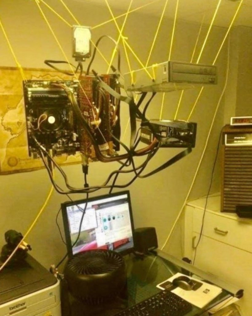 Photo of a computer entirely with a case that has been tethered to the ceiling above the desk with string. Everything is just dangling in the air, like a Scotsman in a kilt.