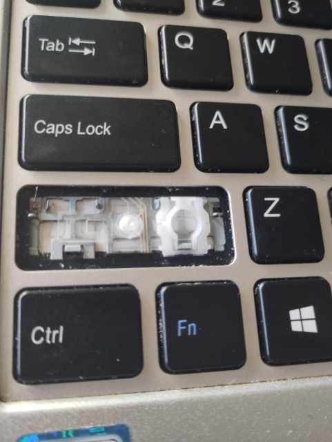 Part of a laptop keyboard with the shift key in focus that had its cover and one of the two hinges removed for cleaning.