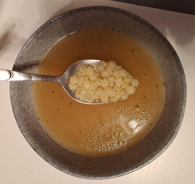 a little bowl with soup.
a spoon is held over it, it contains little star-shaped noodles