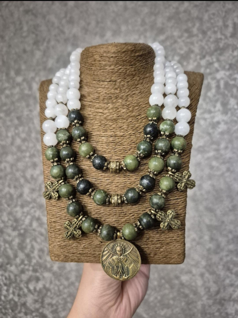 The photo shows a triple necklace, white and green, made of natural stones, a central bronze pendant and two crosses on both sides of the central pendant.
