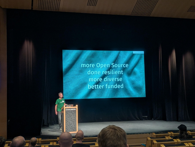 Daniel presenting at foss-north in front of a slide saying "more Open Source, done resilient, more diverse, better funded"