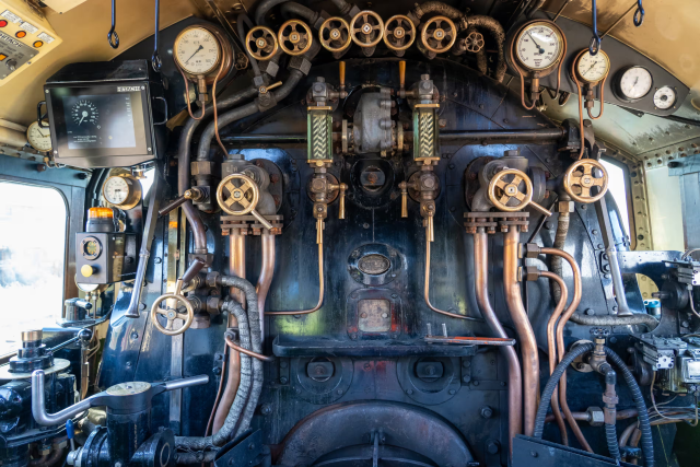 A photo of the cab of a steam locomotive. Alongside all the pipes and valves is a Hitachi ETCS DMI (touchscreen display).