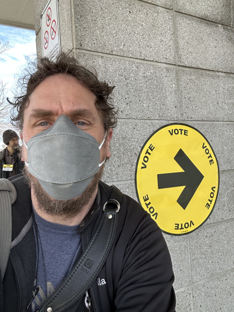 Me wearing a face mask next to a sign indicating the polling place to vote in the Federal election.