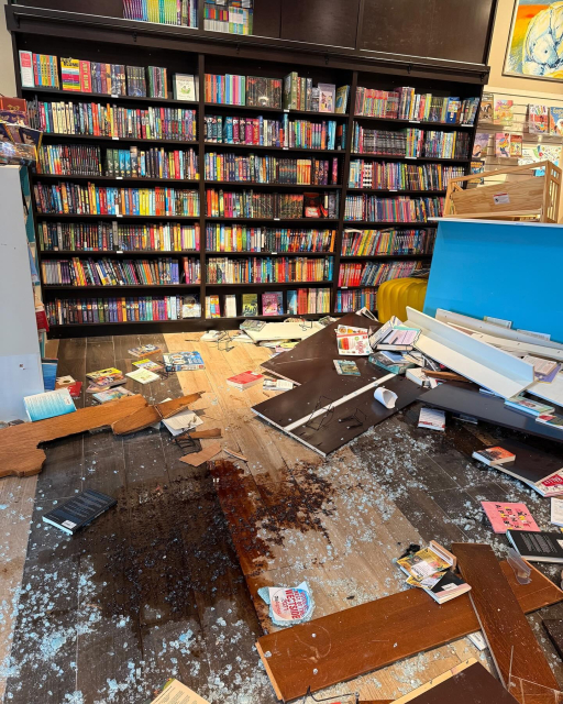 Bookstore damage, with oil stain on the floor and bookshelves broken. Broken glass and books scattered across the floor.
