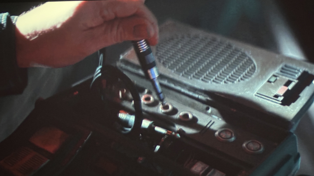 Screenshot from Andor s2e3 with Cassian plugging a headphone jack into a radio. 