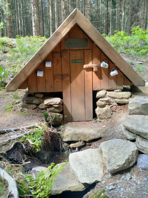 Studánka Slavěna 
Malý dřevěný přístřešek studánky. Po stříškou ve tvaru A jsou na každé straně zavěšeny 2 hrníčky