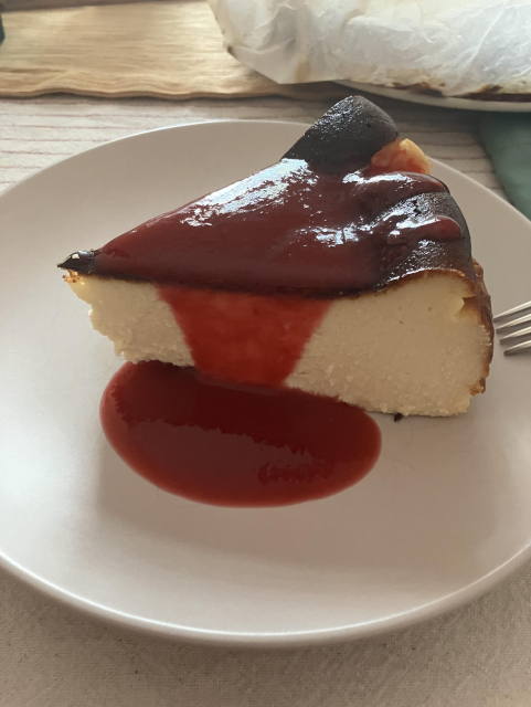 A slice of burnt Basque cheesecake on a plate, with raspberry coulis dripping on it