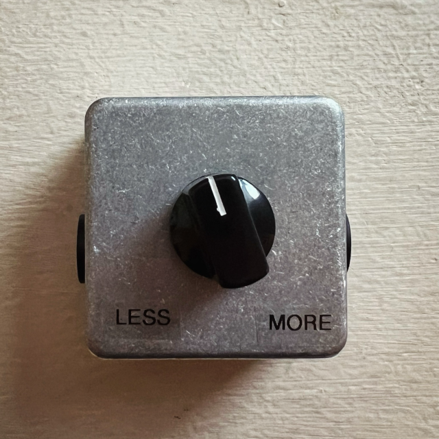 Metallic electronic wall plate with a circular knob actuating between the labels of “less” (-135 °) and “more” (+135°). The dial positioned (-15 °) towards the less position.

