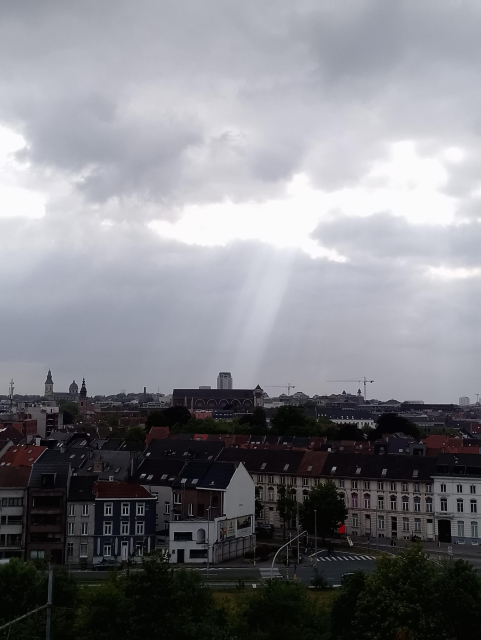 Een panorama van Gent onder een bewolkte hemel. De boekentoren wordt verlicht door een lichtstraal