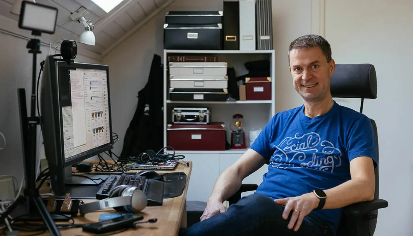 Smiling Daniel in blue tshirt sitting in front of his work desk and keyboard