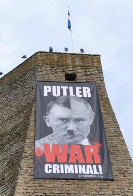 Huge Poster hung from a castle turret in Estonia. An image mixing Putin and Hitler's face together. Text reads 'Putler. War Criminal.

Image by propastop.org