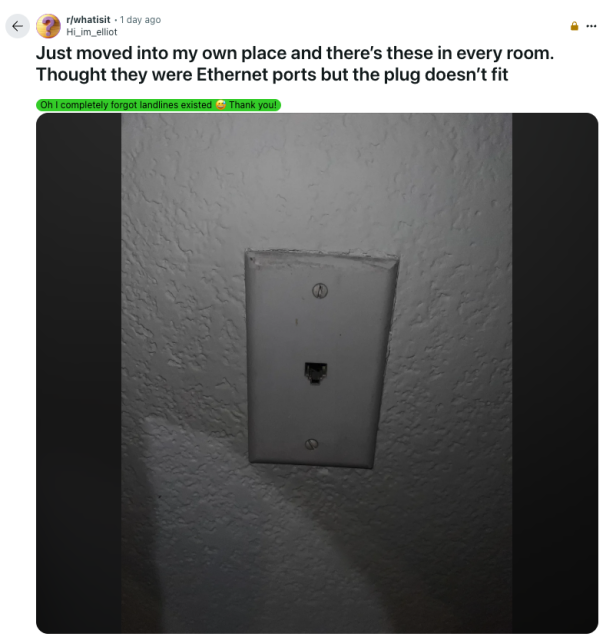 A Reddit post from the subreddit r/whatisit by user Hi_im_elliot. The post reads: “Just moved into my own place and there’s these in every room. Thought they were Ethernet ports but the plug doesn’t fit.” The image below shows an old-fashioned wall plate with a single RJ11 phone jack, commonly used for landline telephones, mounted on a white textured wall. A green highlighted comment above the photo reads: “Oh I completely forgot landlines existed 🥴 Thank you!”
