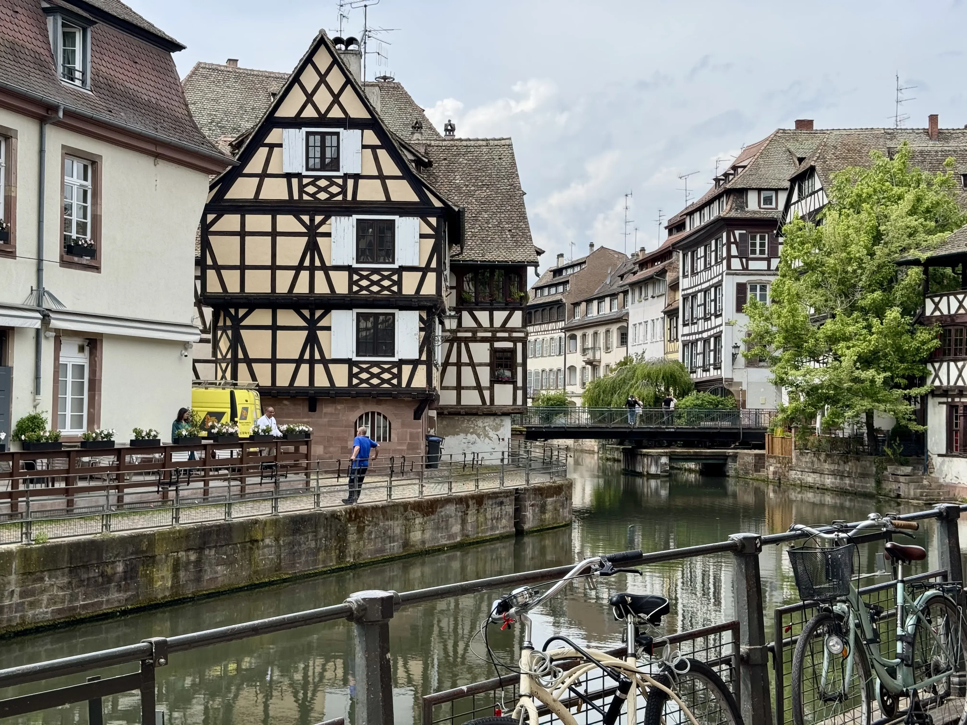 A quiet street in Strasbourg's city center. Houses are half-timbered. There are bicycles parked in the foreground. There's a small bridge crossing the narrow river in the background. It looks very quiet.