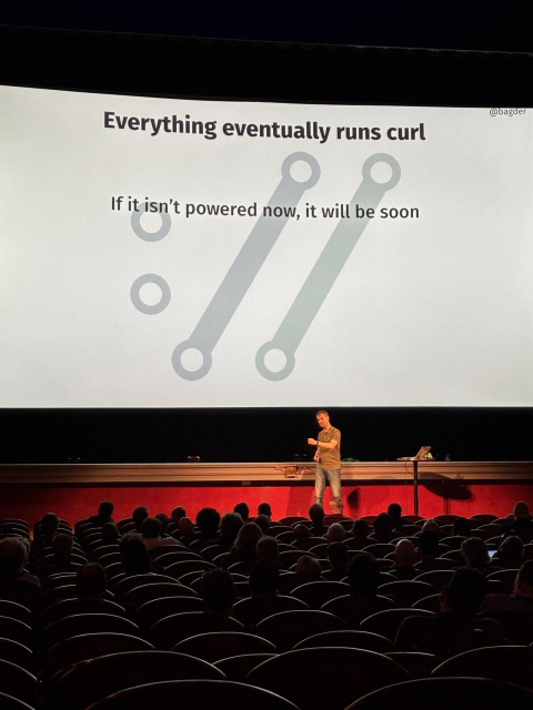 Daniel in front of a big screen showing the curl symbol and the title of the slide says "Everything eventually runs curl"