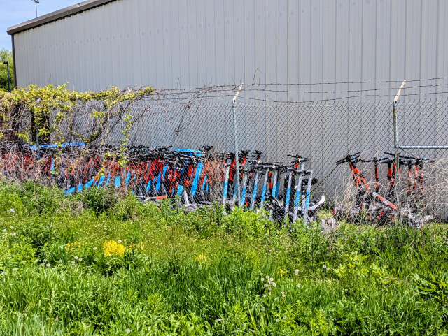 A bunch of electric rental scooters along the side of a warehouse building