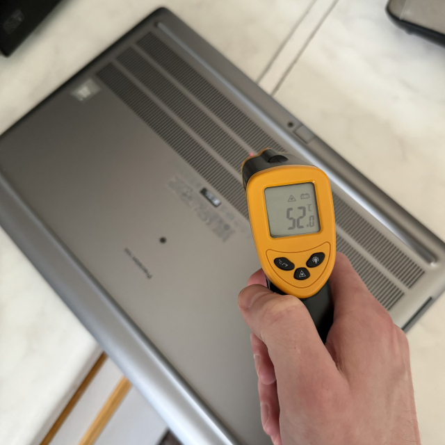 Image of a laptop on a kitchen countertop. There’s an infrared thermometer pointing at it ans reading 52 degrees Celsius.