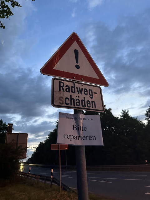 Ein Verkehrsschild mit "Achtung Radwegschäden" und darunter ein laminierter Hinweis mit der Notiz "Danke für den Hinweis, bitte reparieren"
