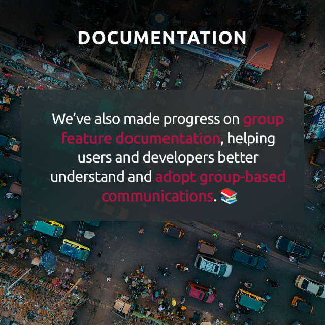 Aerial view of a busy urban intersection with cars, vendors, and people. Overlaid text reads: “We’ve also made progress on group feature documentation, helping users and developers better understand and adopt group-based communications.” Key phrases are highlighted in pink, and a book emoji appears at the end.