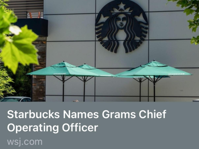 Starbucks logo (a stylized drawing of a mermaid wearing a crown in a circle) on a building’s exterior walls, some table umbrellas and a tree visible as well. Below this, a headline reads, “Starbucks Names Grams Chiefs Operating Officer” and the name of the source, wsj.com.